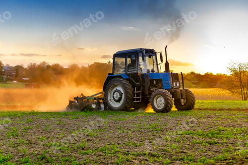 Preview: Modern blue tractor machinery plowing agricultural field meadow at farm at spring during sunset