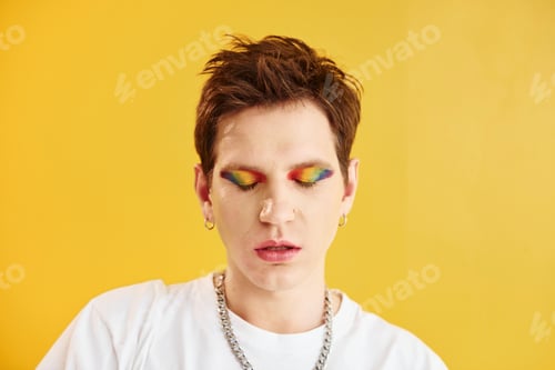 Preview: Young gay man is standing in the studio and posing for a camera. Against yellow background