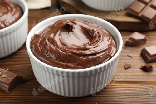 Preview: Tasty pudding in bowls and pieces of chocolate on wooden table, closeup