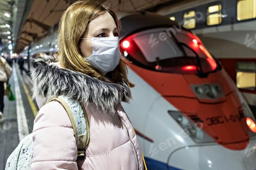 Preview: A woman in a mask stands on the platform waiting for the departure of a high-speed train.