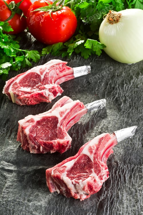 Three Raw Lamb Chops with Vegetables on Slate