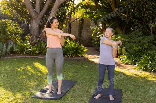 Preview: Stretching on yoga mats, asian grandmother and granddaughter exercising together in outdoor garden
