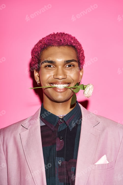 Preview: portrait of joyful young man with white rose in mouth smiling at camera and acting like doll