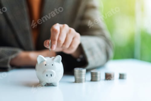 Preview: A businesswoman putting coin into piggy bank with coins stack on the table for saving money