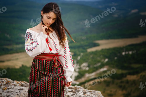 Preview: Attractive woman in traditional romanian costume on mountain green blurred background.
