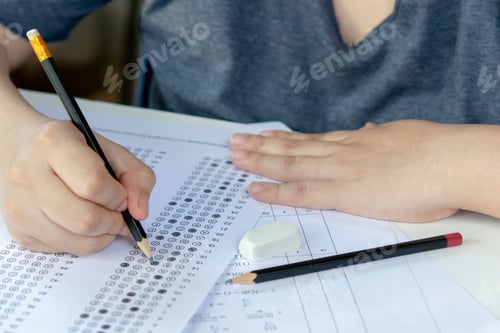 Preview: Students hand holding pencil writing selected choice on answer sheets