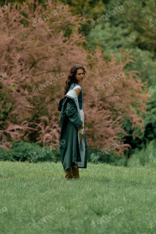 Preview: Curly haired woman in stylish raincoat enjoys a vibrant outdoor setting during summer