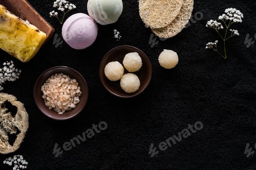 Preview: top view of handmade scrub, sea salt and small white flowers on black background