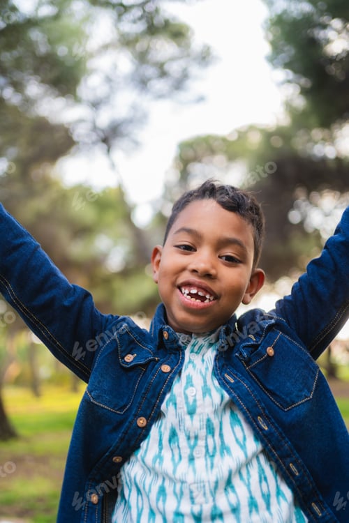 Preview: Happy boy smiling and raising arms outdoors