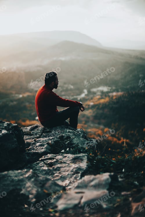 Preview: Young man sitting in a very high place on a sunset thinking and he’s wearing red sweater