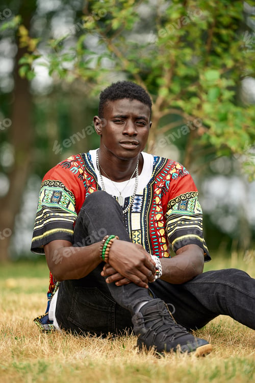 Preview: A black man is resting in the park, an attractive black man is sitting on the grass in the fresh air