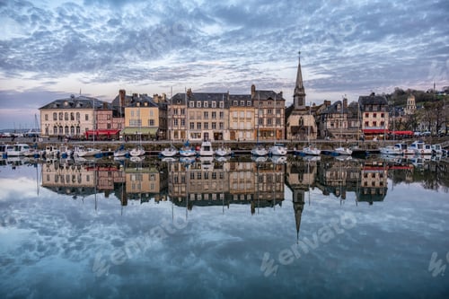 Preview: Port of Honfleur with the buildings reflecting on the water under a cloudy sky in France