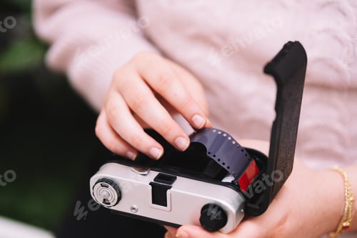 Preview: Girl in a pink sweater putting film on an analog camera.