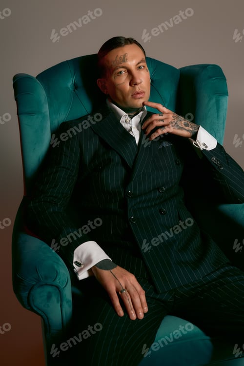 Preview: Handsome stylish man seated elegantly in a striking teal chair, showcasing modern fashion