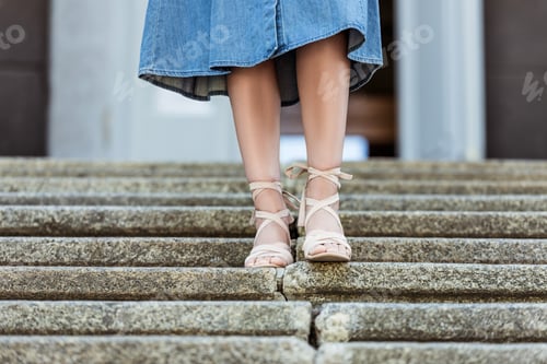 Preview: cropped shot of woman in denim skirt and fashionable shoes walking down steps