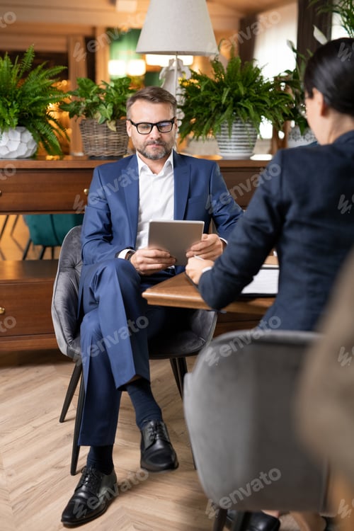 Preview: Busy employee in suit sitting by table in restaurant and scrolling in touchpad