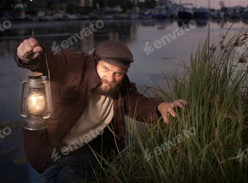 Preview: a man with a beard in vintage clothes and with a kerosene lamp in his hand