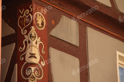 Preview: Carved wooden beam on a historic building, featuring decorative motifs, face mask, and the year 1549