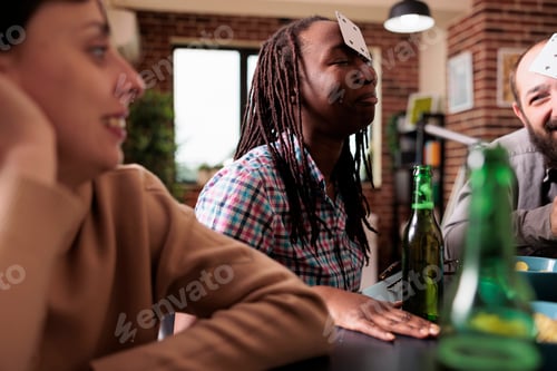 Preview: Happy multicultural group of friends sitting at home while playing guessing card games together.