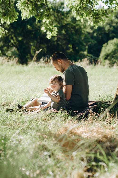 Preview: Boy and Man Reading Outdoors in Grassy Field