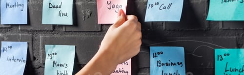 Preview: cropped view of woman attach colorful sticker pads with notes on black brick wall