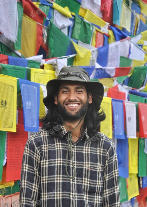 Preview: Photo of a male tourist looking at camera while smiling, standing against Buddhist prayer flags