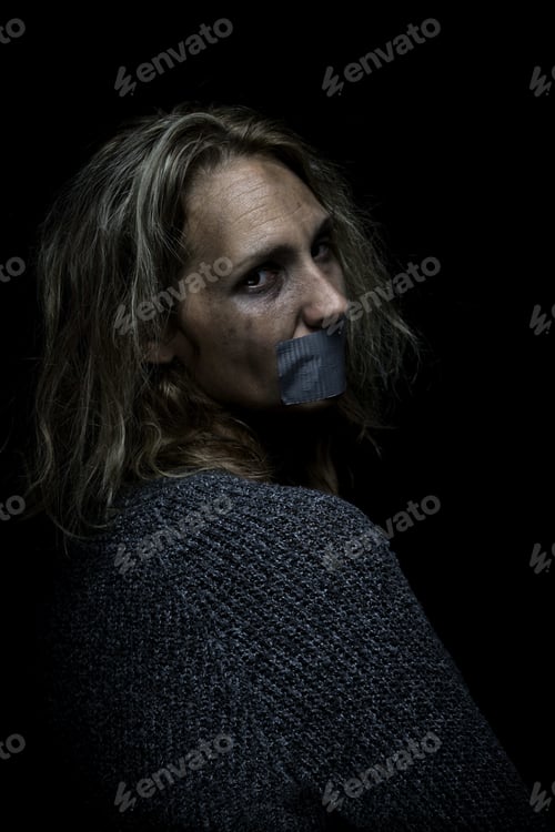 Preview: Vertical shot of an abused and scared woman on black background silenced with tape