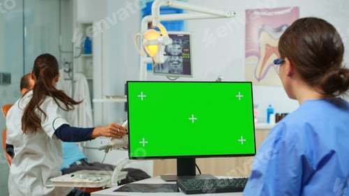 Preview: Nurse looking at green screen display while doctor examining patient