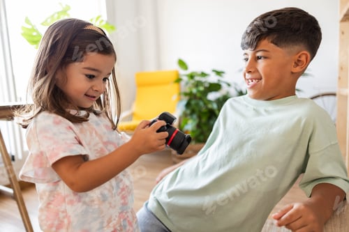 Preview: Smiling siblings embrace while looking at a camera, enjoying a fun moment together at home.