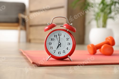 Preview: Alarm clock, yoga mat and dumbbells on wooden floor indoors. Morning exercise