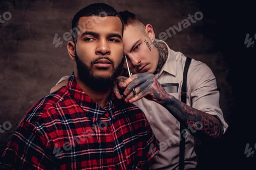 Preview: Old-fashioned professional tattooed hairdresser does a haircut to an African American client.