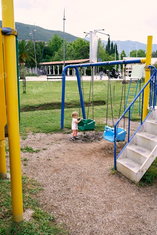 Preview: Little girl holds on to the swing with her hands on the background of buildings and park