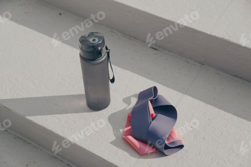 Preview: Gray sport bottle drinking water flask and gymnastic elastic bands on white stair.