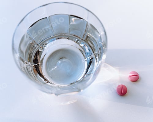 Preview: glass of clean water in rays of light and pills on table