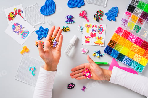 Preview: Children's hands holding a cat and a rabbit made of colorful aqua beads above a workplace