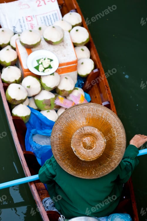 Preview: High angle view of person wearing hat sitting in narrow boat, transporting green coconuts.