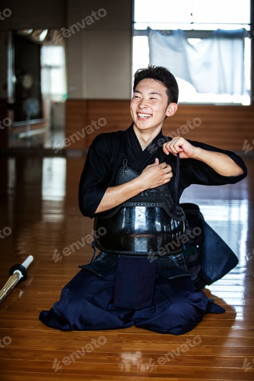 Preview: Male Japanese Kendo fighter kneeling on floor, fastening his breastplate.