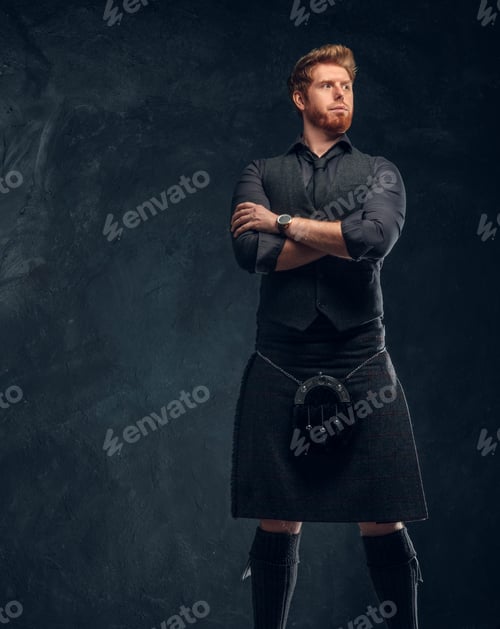 Preview: Redhead man dressed in an elegant vest with tie and kilt in studio against a dark textured wall
