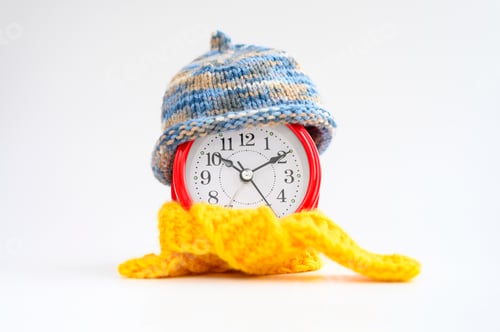 Preview: red round alarm clock in knitted wool blue hat and yellow scarf on a white background