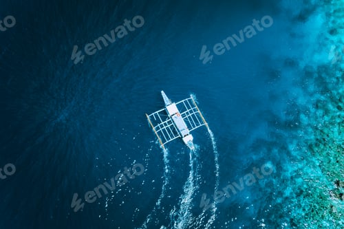 Preview: Aerial drone view of white traditional Filipino boat floating on top of clear blue water surface. El