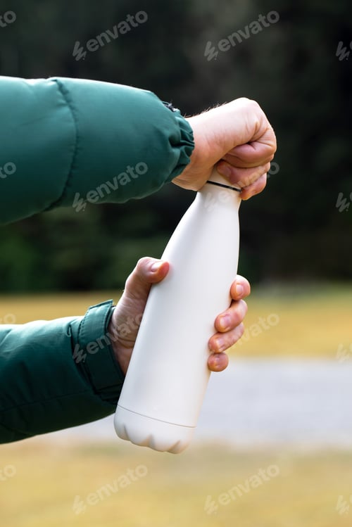 Preview: man holds mockup thermos against blurry bushes closeup