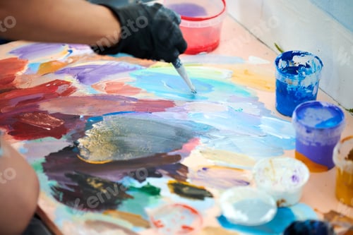 Preview: Artist hand in black gloves holds paint brush and choose color from colorful palette at art festival