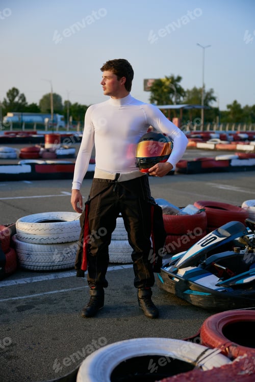 Preview: A go-kart racer stands confidently at the karting circuit wearing racing gear and holding a helmet