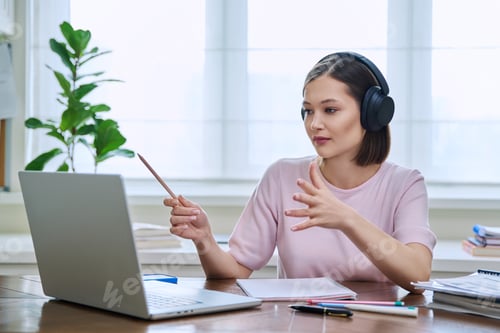 Preview: Young female college student in headphones studying using laptop computer for video chat