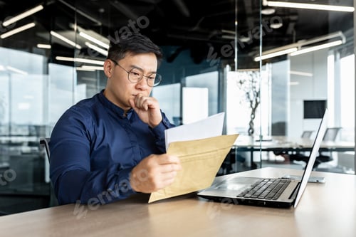 Preview: Thinking asian businessman working inside modern office building, man reading letter received from