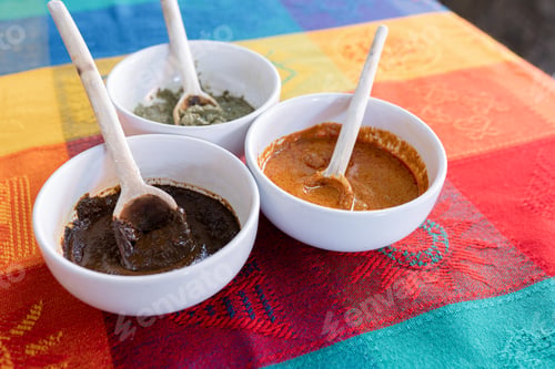 Preview: Three bowls with red, green and yellow mole sauce on top of a colorful traditional tablecloth