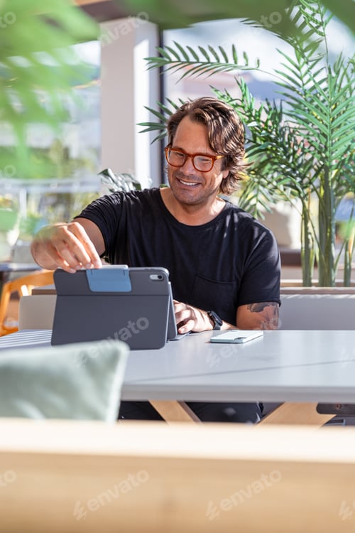 Preview: An hipster man is working using tablet and smiling, vertical photo.