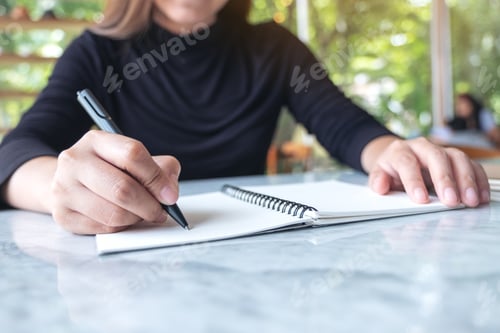 Preview: Closeup image of business woman writing on blank notebook on table with green nature background