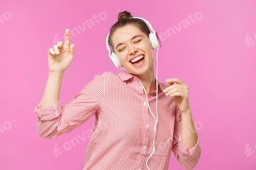 Preview: Young woman dancing to sounds of favorite music she is listening to through white headphones