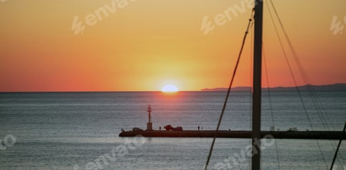 Preview: Sunset over Tinos island, Cyclades, Greece. Ship mast, beacon silhouette golden sun dives into sea.